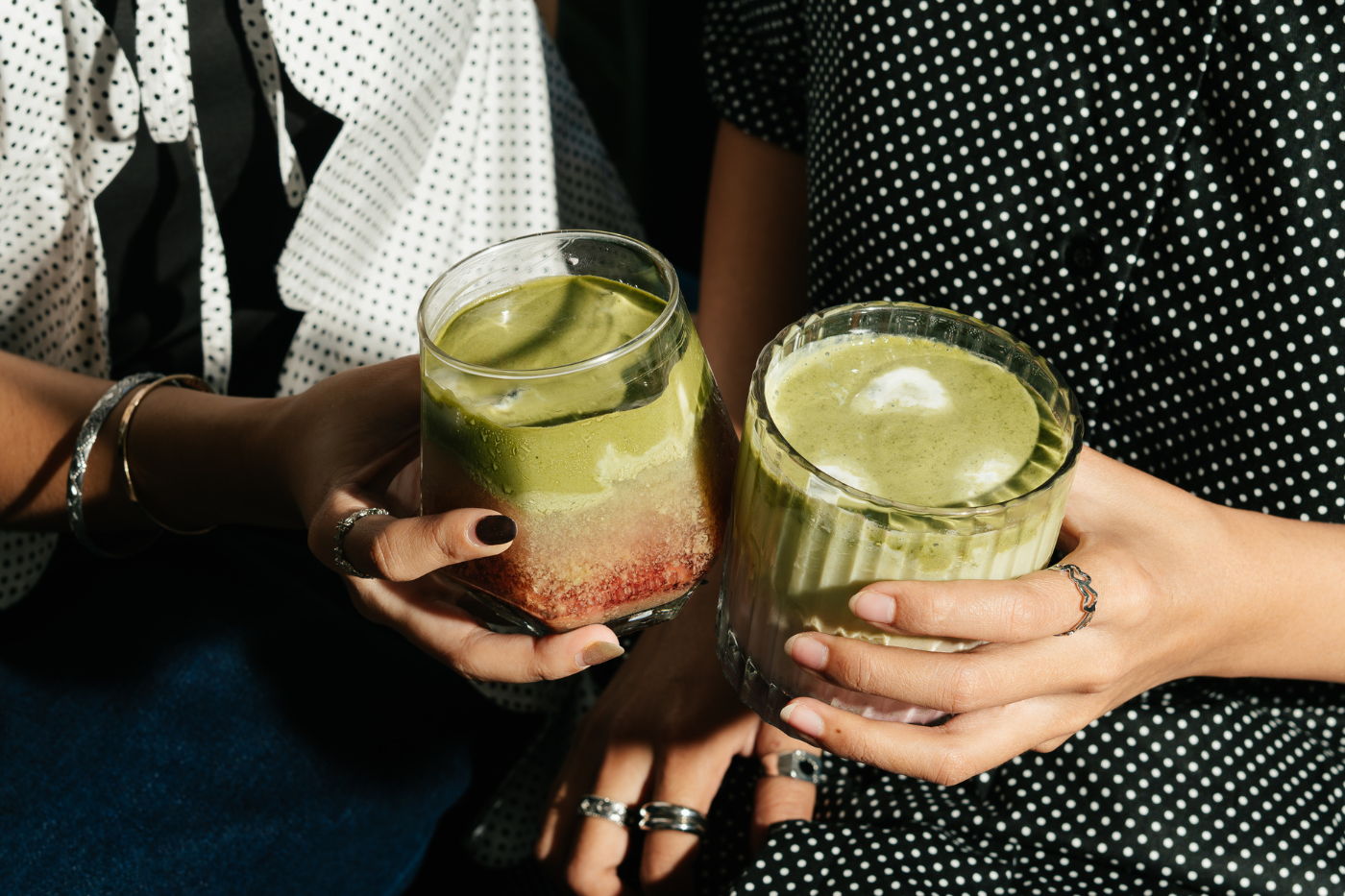 Two hands holding glasses of green beverages in a stylish setting.