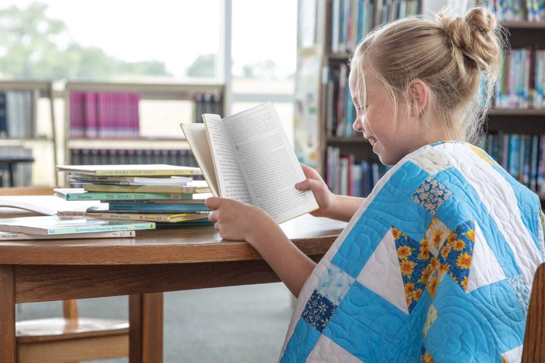 child reading book while wearing quilt