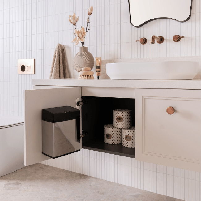 Modern bathroom with open cabinet, trash can, and decorative items.