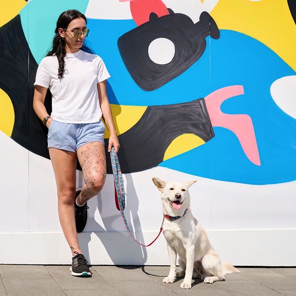Person standing with a dog in front of a colorful mural.