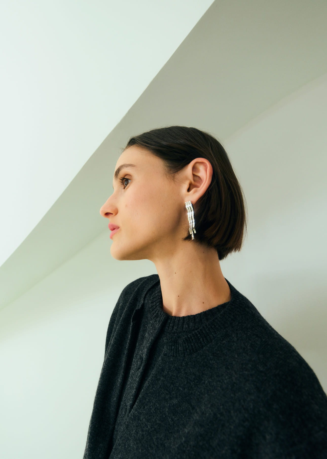 Profile of a woman with short hair wearing earrings against a minimalist background.