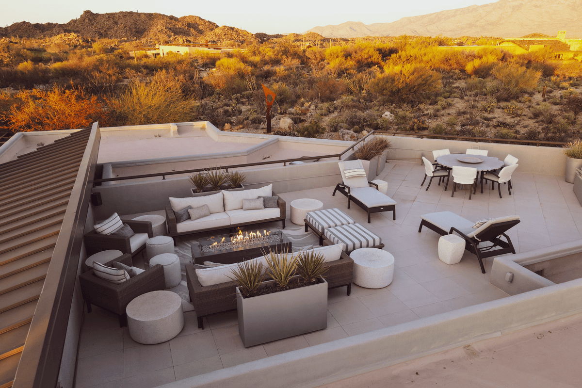 Rooftop desert patio with outdoor fire pit seating, dining area, chaise lounges, and mountain views.