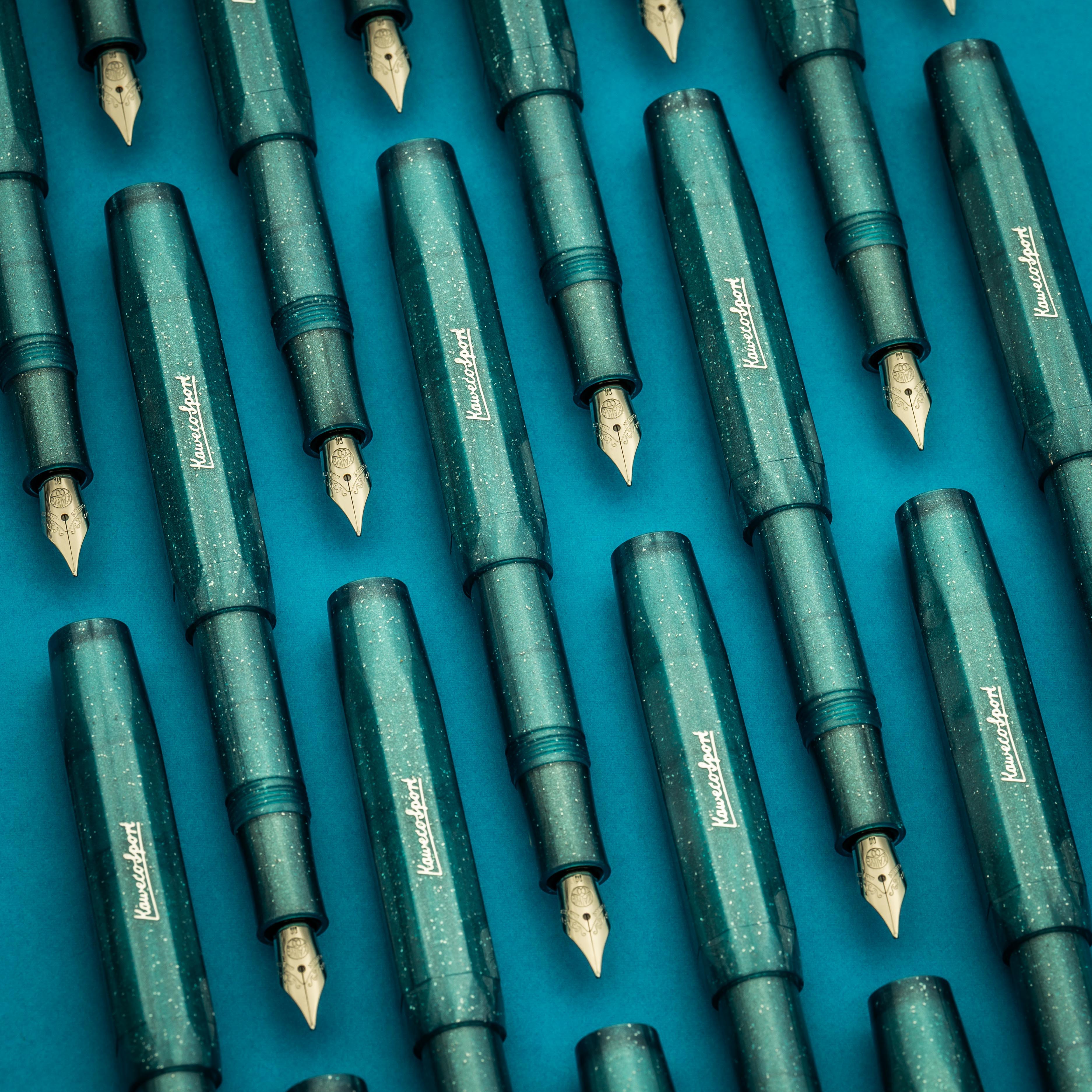 A photo of many Kaweco fountain pens of the same turquoise color arranged on a blue surface