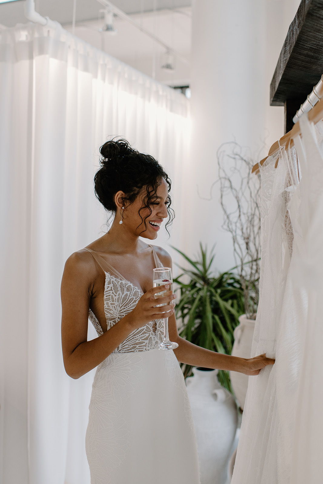 A woman in a wedding dress holding a glass, admiring bridal gowns.