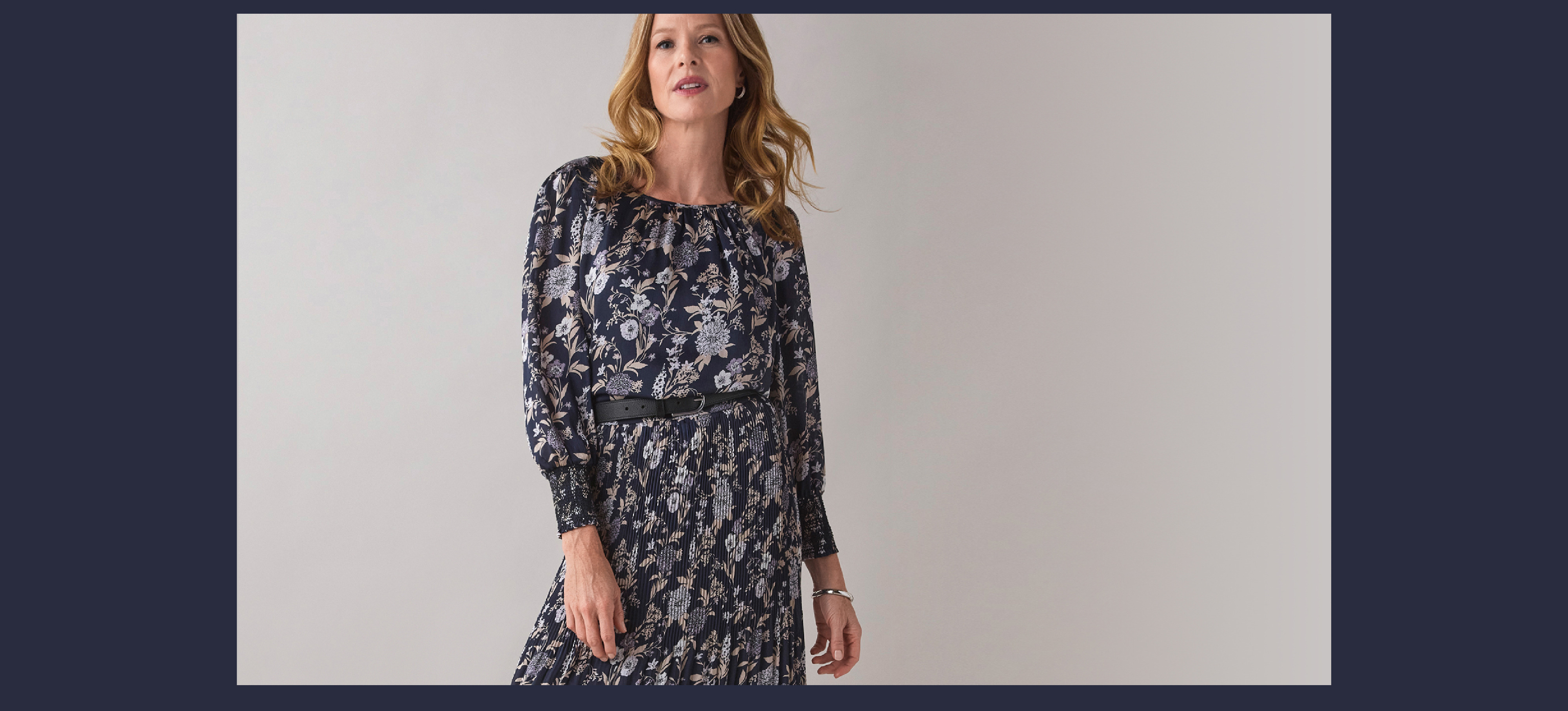 Woman wearing a patterned dress, standing against a neutral background.