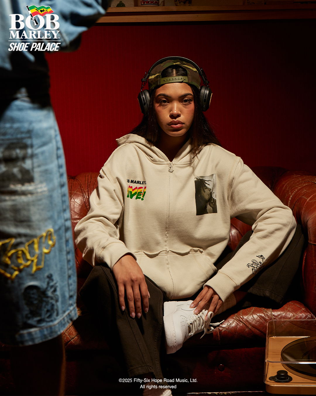 Young person in a hoodie, sitting on a couch, wearing headphones.