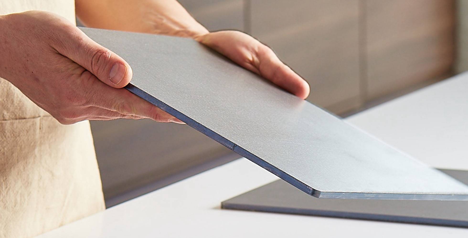 A chef holds a Misen Oven Steel in both hands with its edge facing the camera, showing its 6mm thickness.