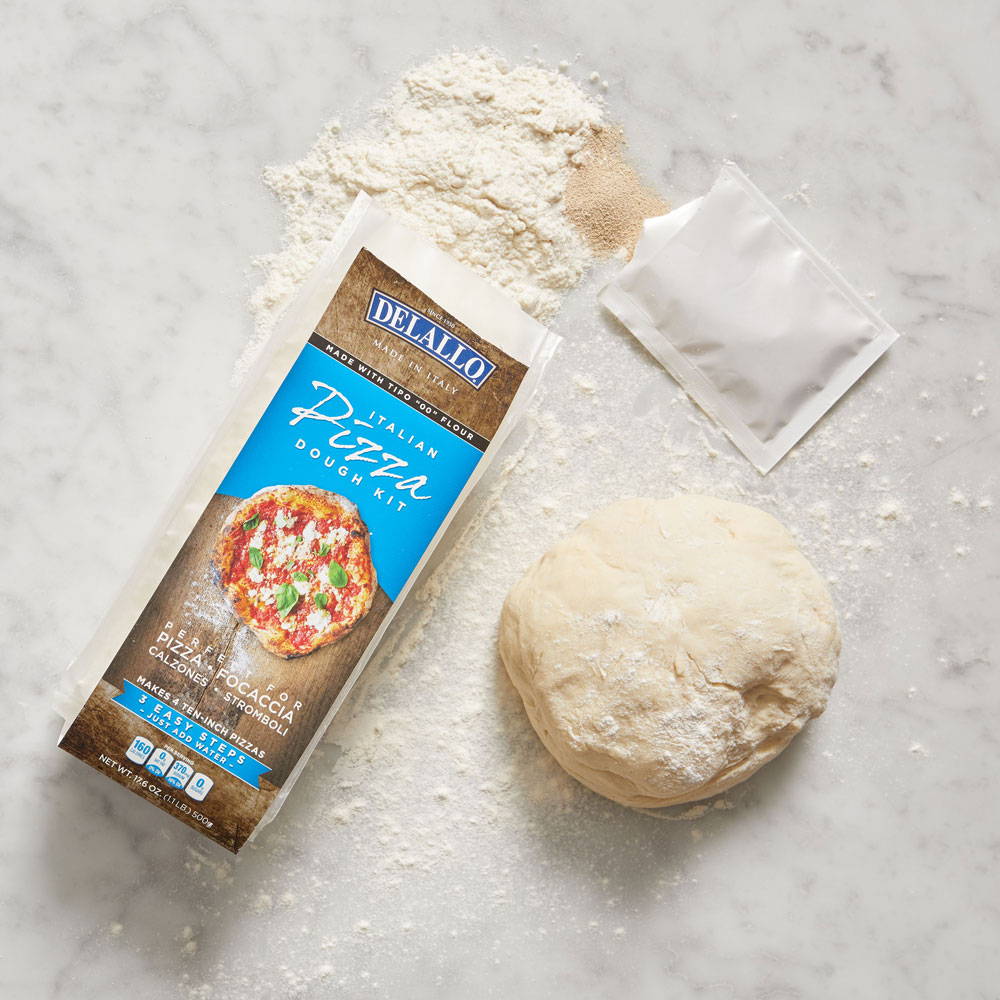 Package of DeLallo Pizza Dough Kit on a marble table next to a ball of dough