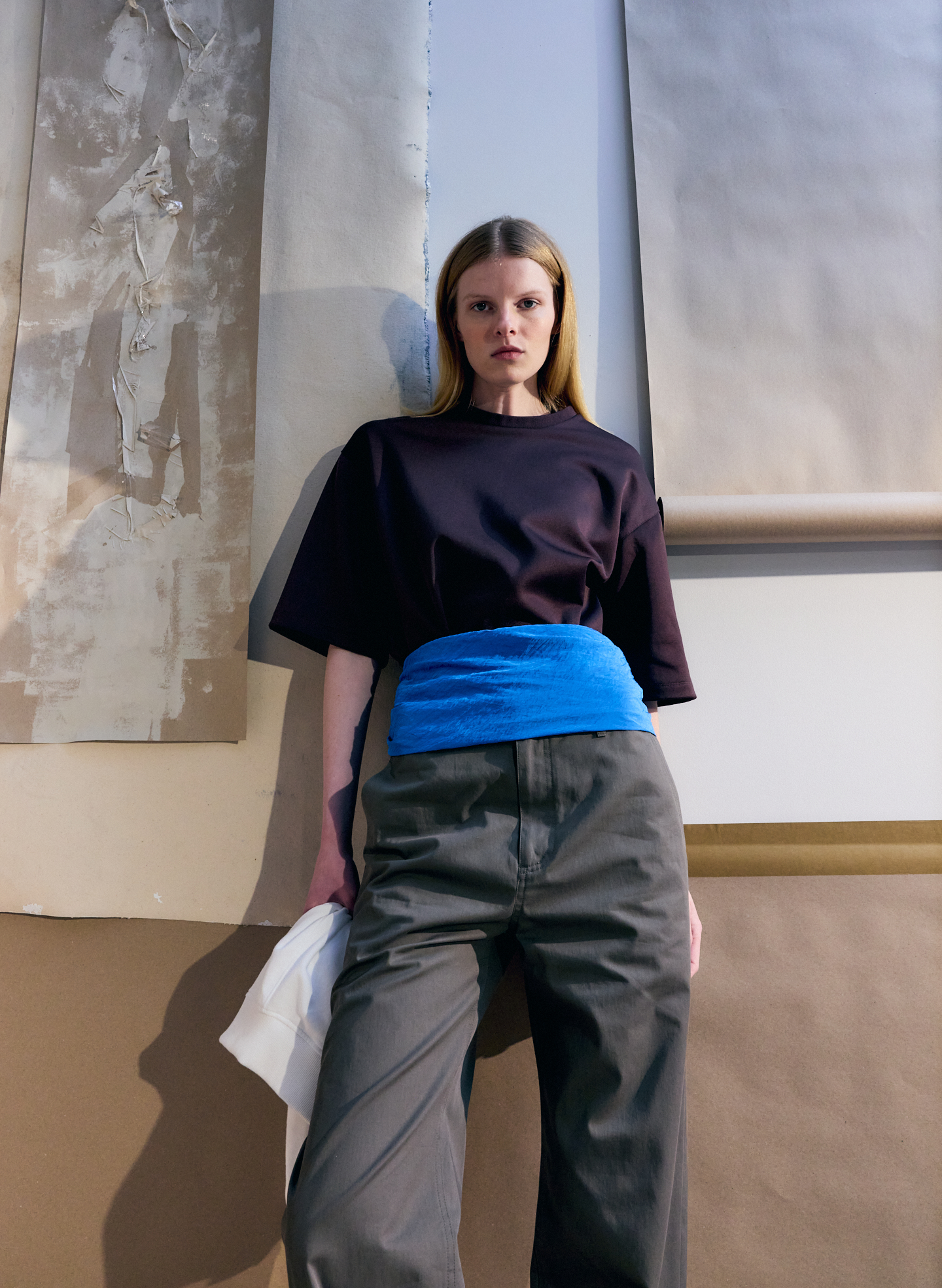 Model wearing a black top and gray pants with a blue belt.