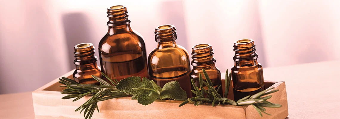 Five amber glass bottles arranged in a wooden holder with greenery.