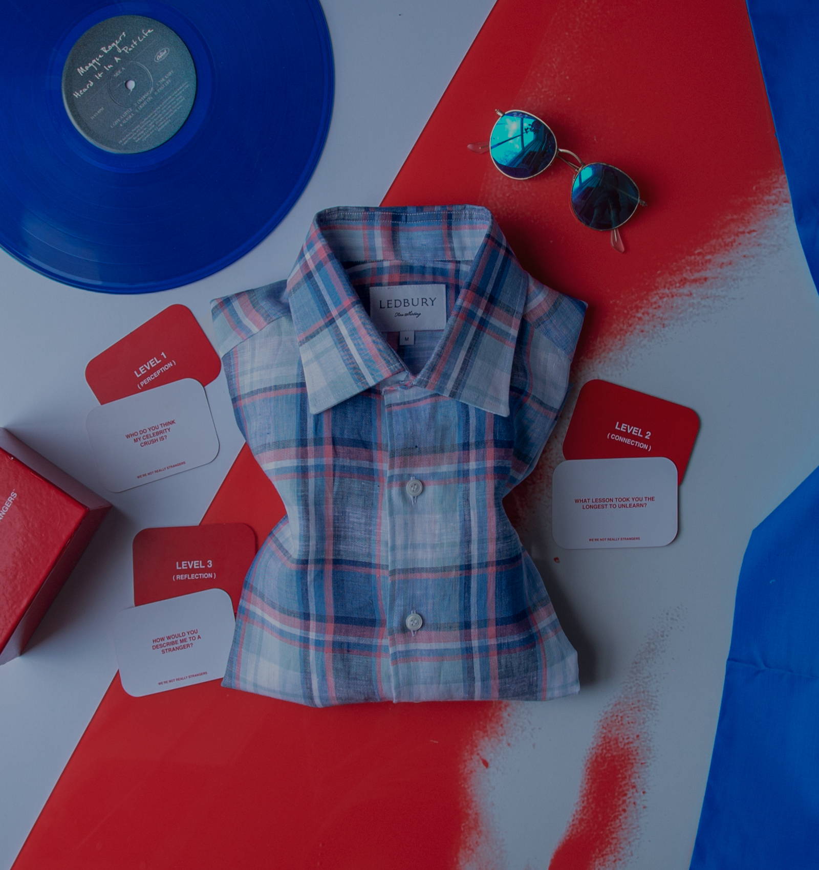 The Cerulean Blue Deacon Linen Plaid Casual Shirt surrounded by card games, a record and sunglasses