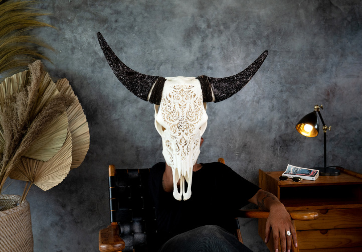 A man is sitting on a chair and is holding the carved horns cow skull Tribal #2.