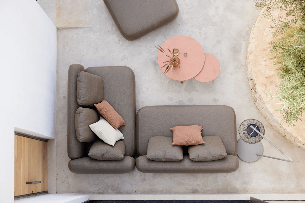 Overhead view of a modular outdoor sectional with neutral cushions and accent pillows, paired with round side tables on a minimalist patio.