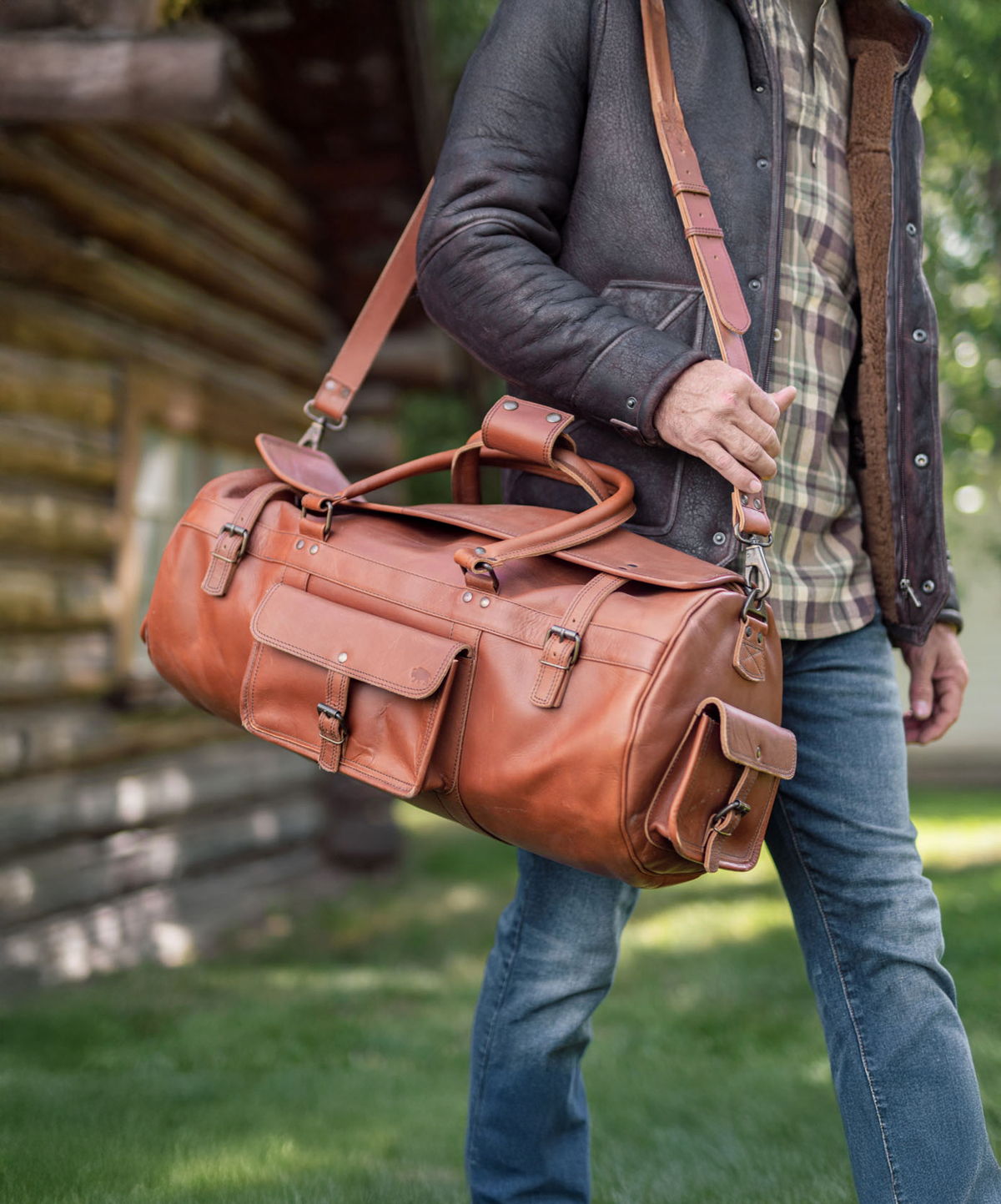 Man carrying a Buffalo Jackson full-grain leather duffle bag by a log cabin