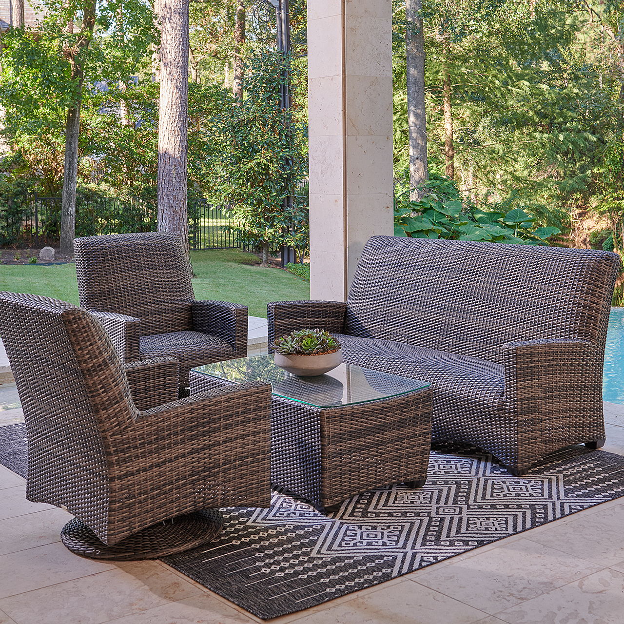 Outdoor seating area with wicker furniture and a glass table.