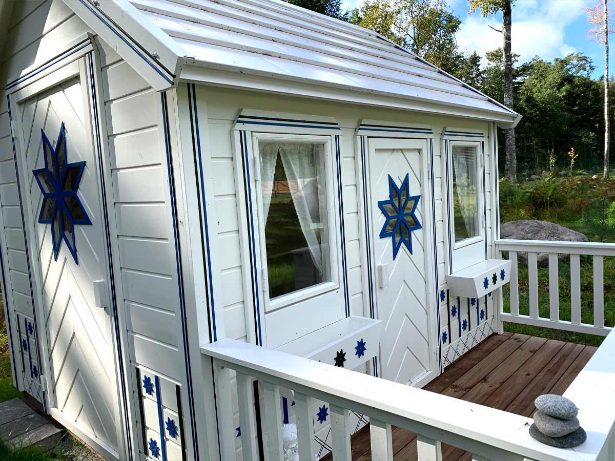 Blue and white fully finished Outdoor Playhouse with white Flower boxes and cornflower shape windows in a backyard by WholeWoodPlayhouses