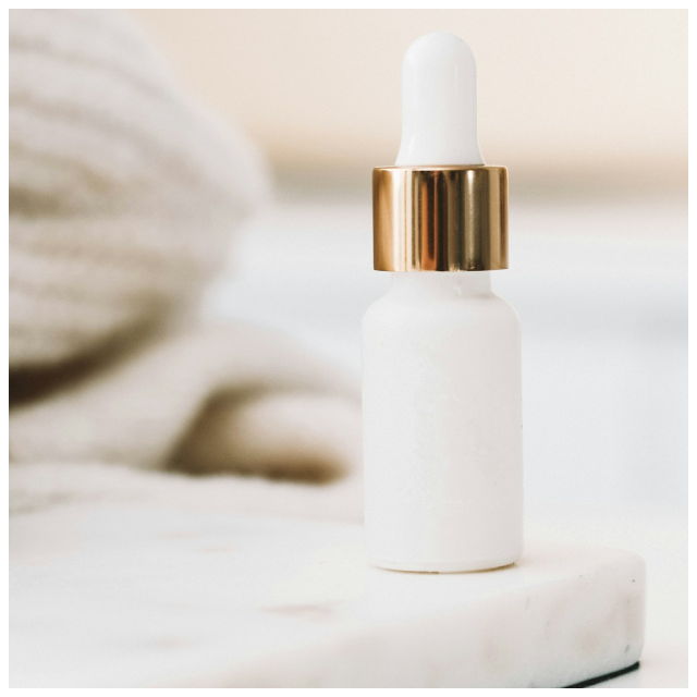 A white makeup bottle, sat on a marble surface, with a towel in the background