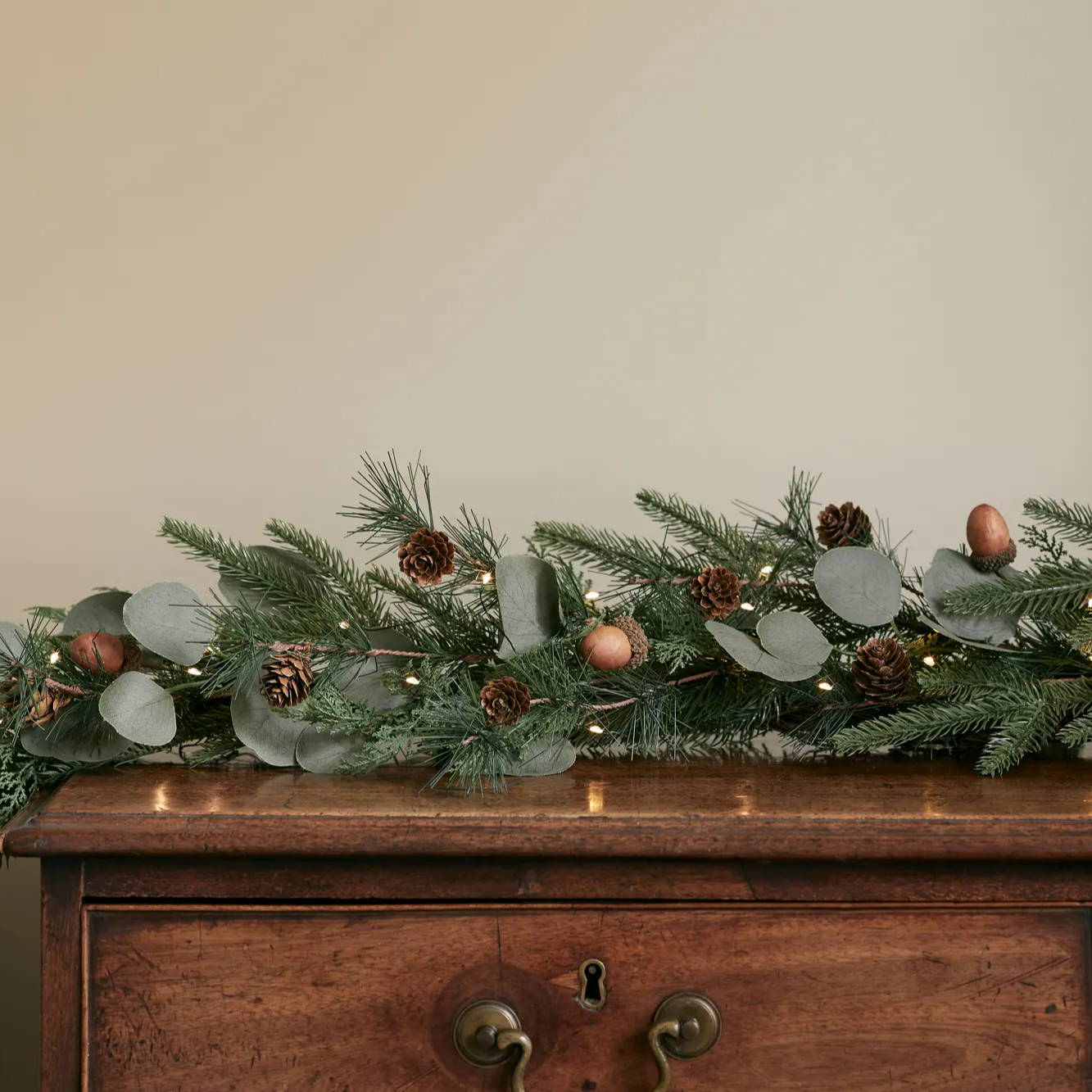 Acorn Christmas garland with micro lights on a wooden cabinet.
