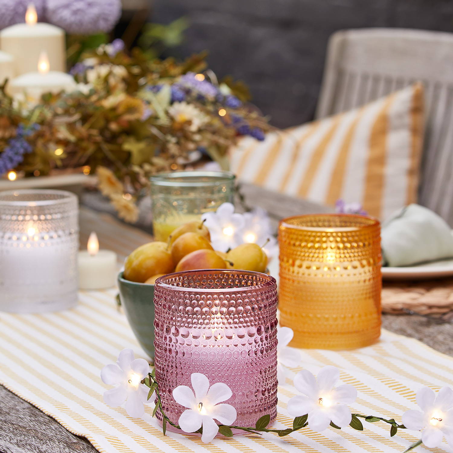 3 colourful LED candles on an alfresco dining table with a flower garland and yellow table runner.