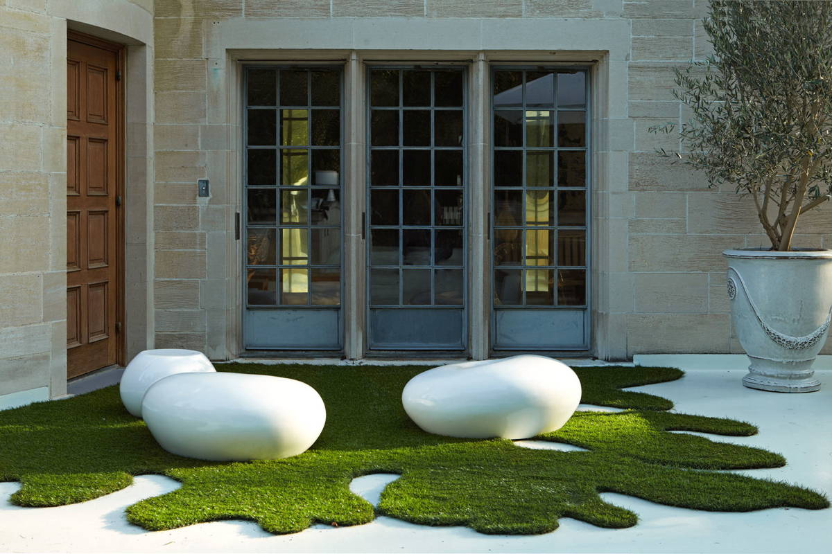 White outdoor pebble seats and table make a statement against an organically shaped bright green turf.
