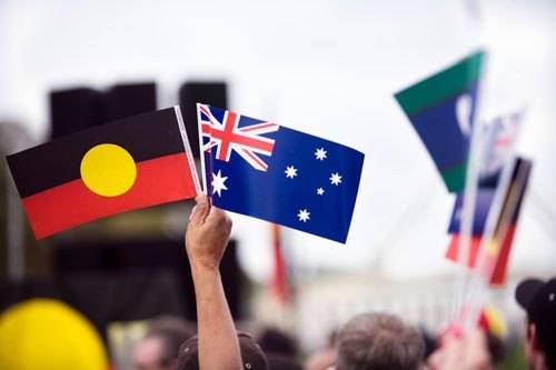 Image of person in crowd holding Aborigional Flag and Australian Flag. 