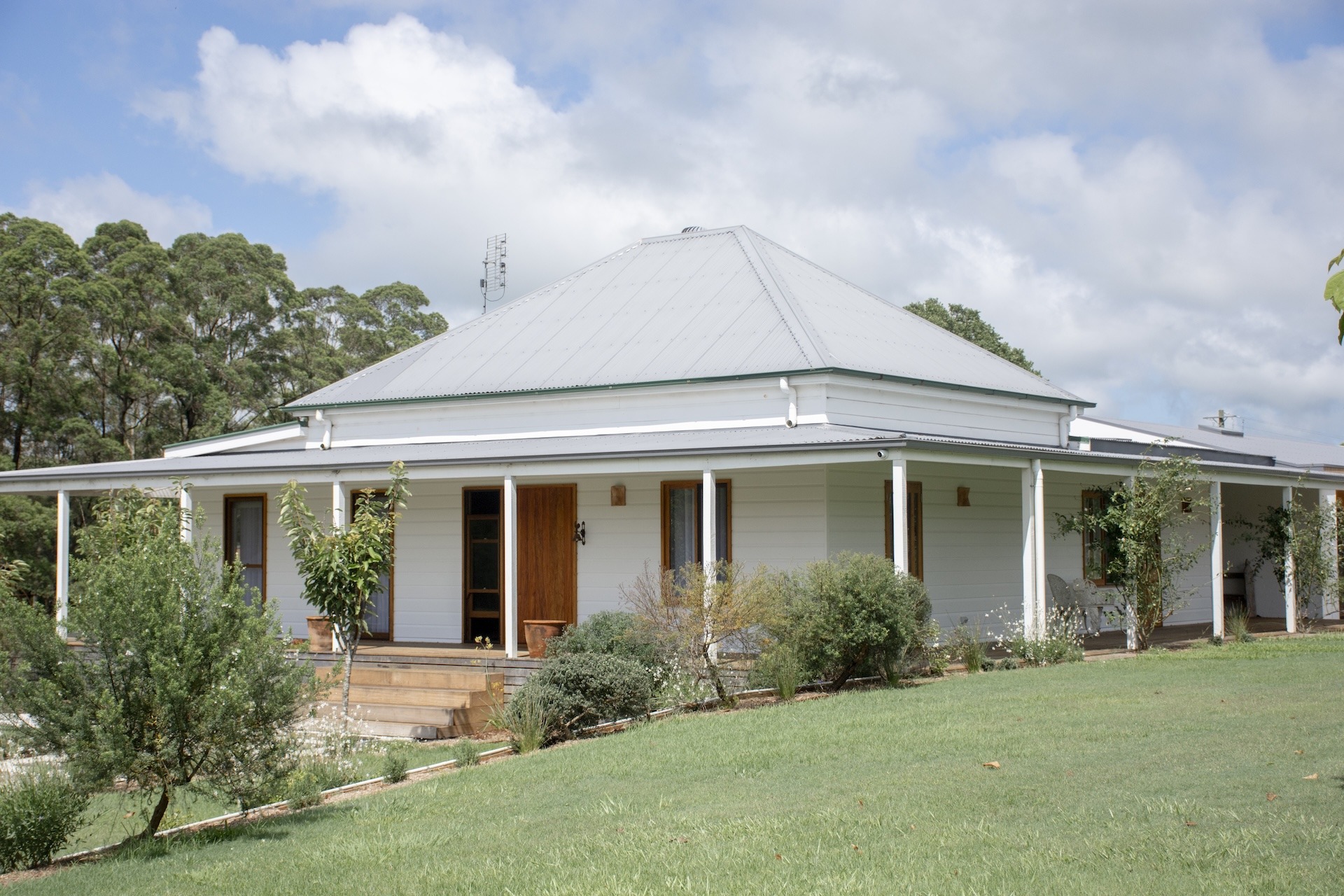 A modern farmhouse building with a porch and surrounding greenery.