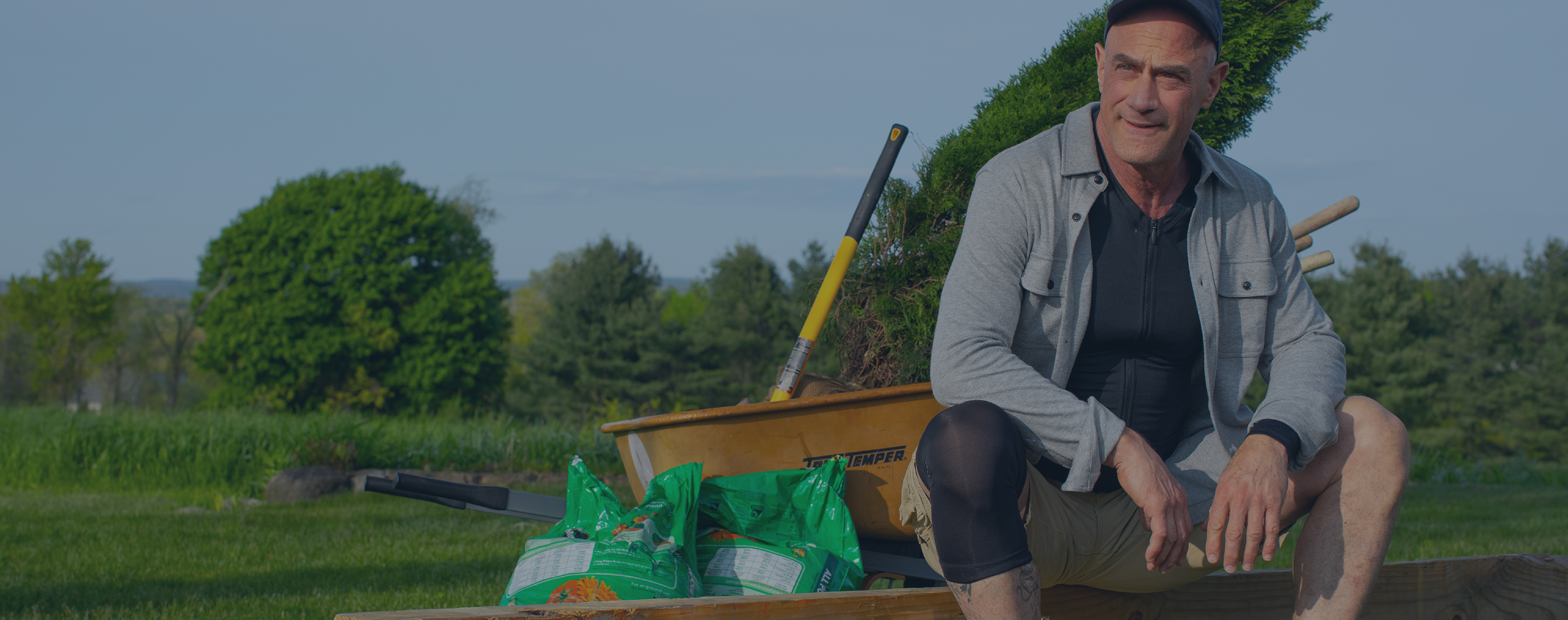 Christopher Meloni doing yard work wearing the Full Back Support Shirt and Compression Knee Sleeve