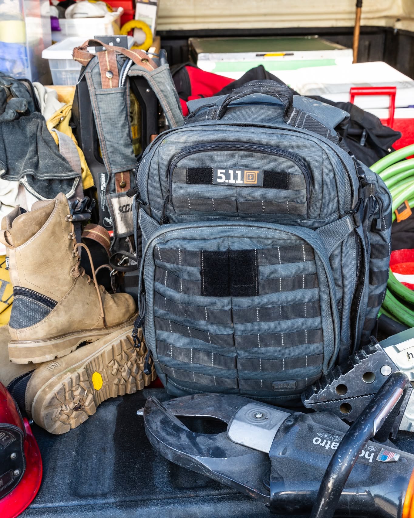 A black tactical backpack next to work boots and various tools.