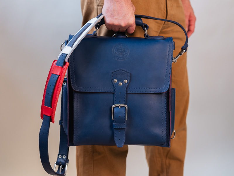 A person holding a navy blue leather bag with a shoulder strap.