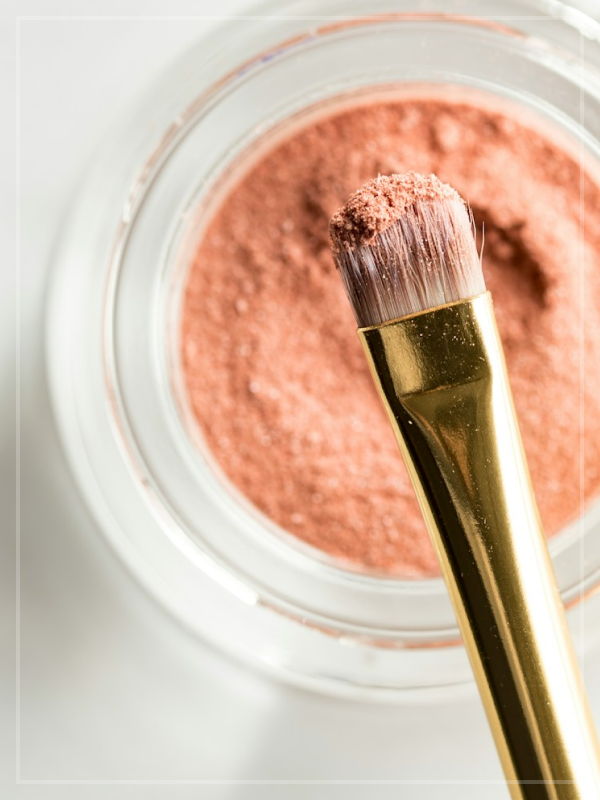A makeup brush over a pot of makeup powder