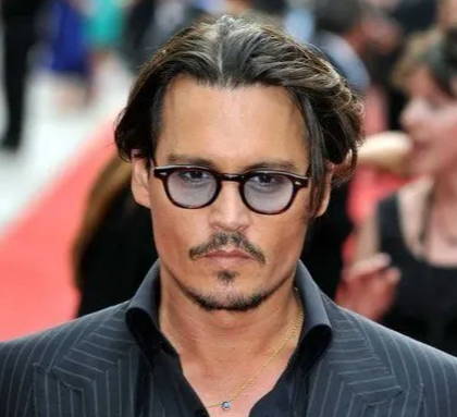 Johnny Depp porte des lunettes rondes emblématiques à monture noire avec une teinte bleue et une chemise noire avec une veste rayée