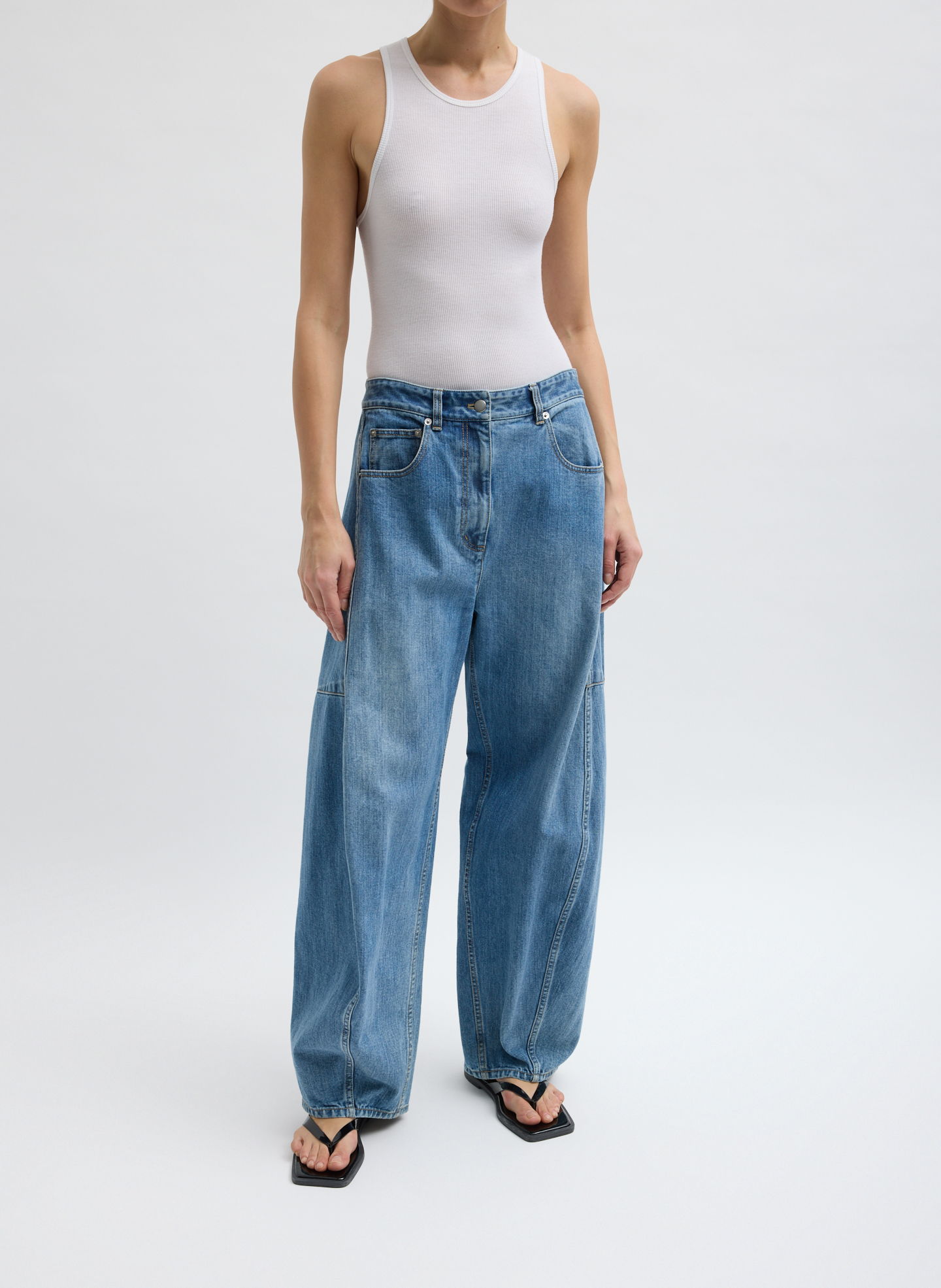 Person wearing a white tank top and baggy blue jeans.