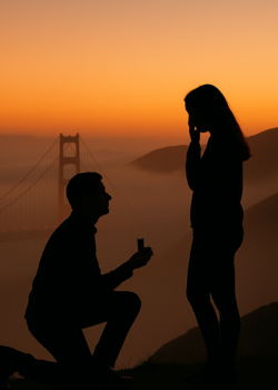 Silhouetted man proposing at sunset, creating a romantic engagement moment outdoors.