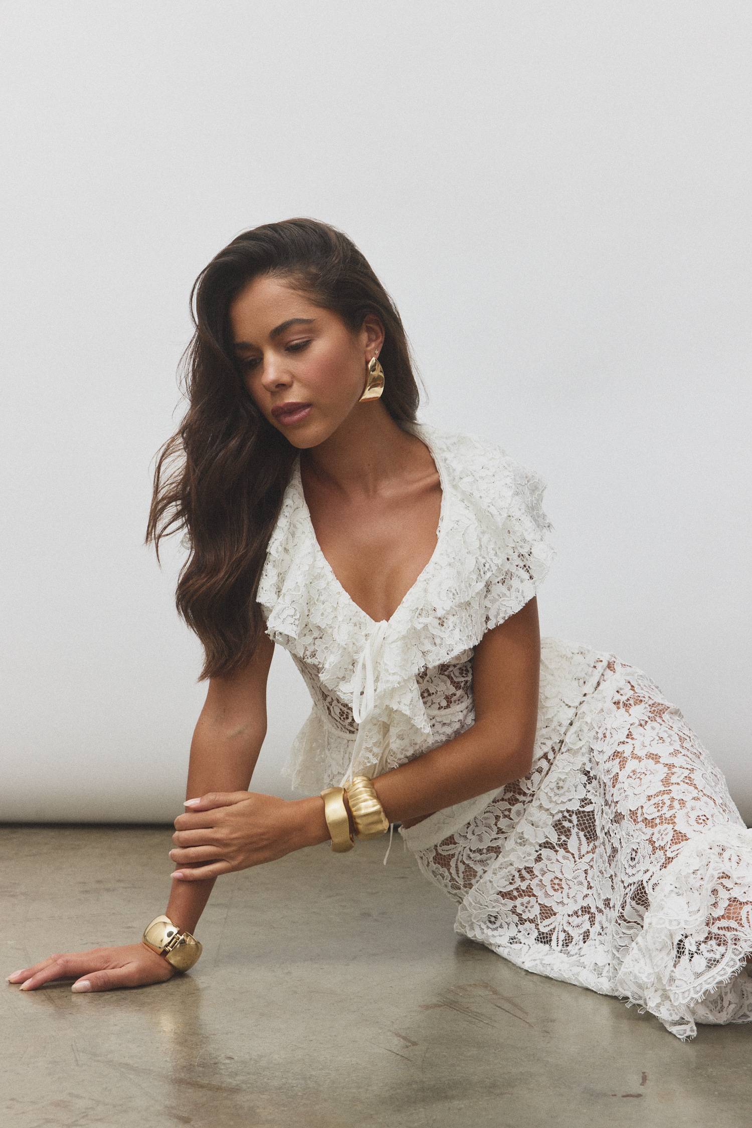 Woman in a white lace dress posing gracefully on the floor.