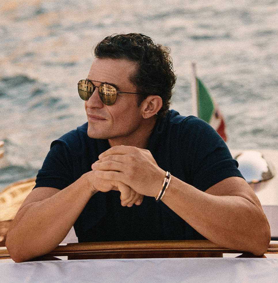 Man with sunglasses leaning on a boat railing by the water.