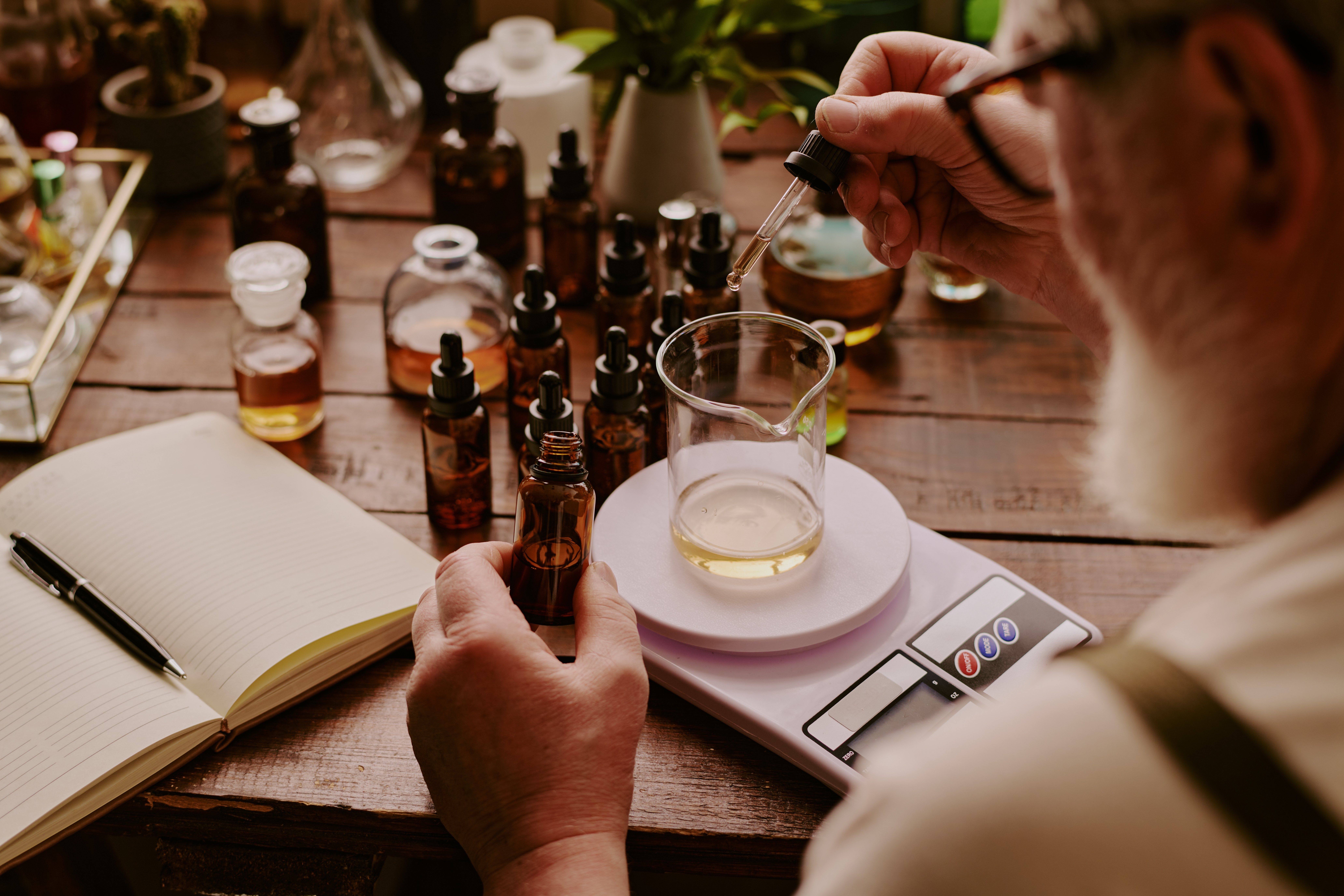 Person measuring liquid ingredients for a potion or remedy with various bottles.