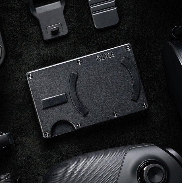 A black wallet among various accessories on a dark surface.