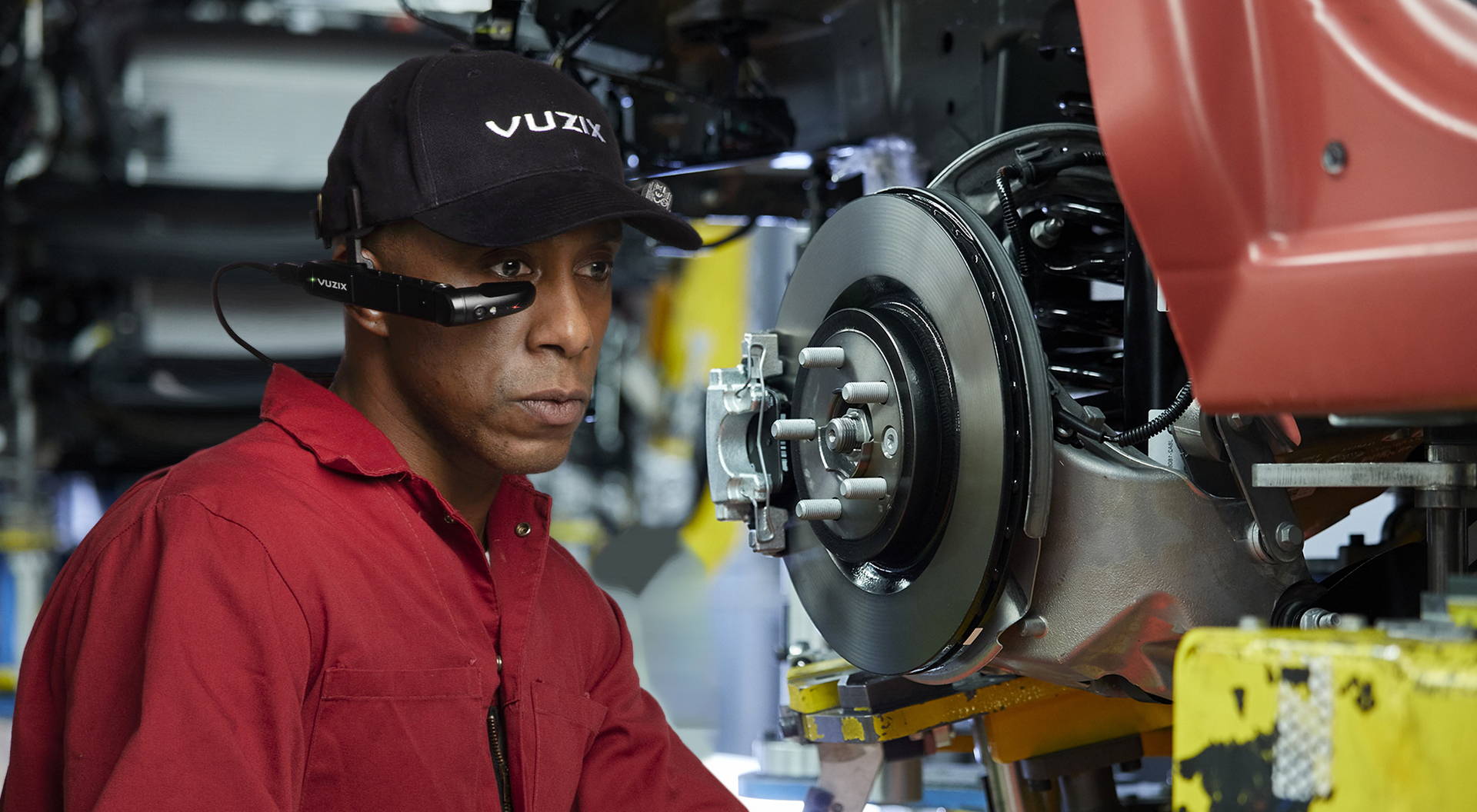 African American man in red collared shirt wearing Vuzix cap and smart glasses as he operates manufacturing equipment.