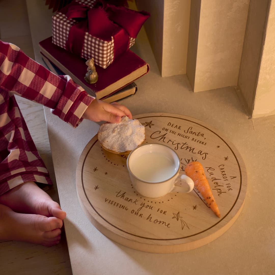 A child’s hand places cookies and milk for Santa on a decorative plate.