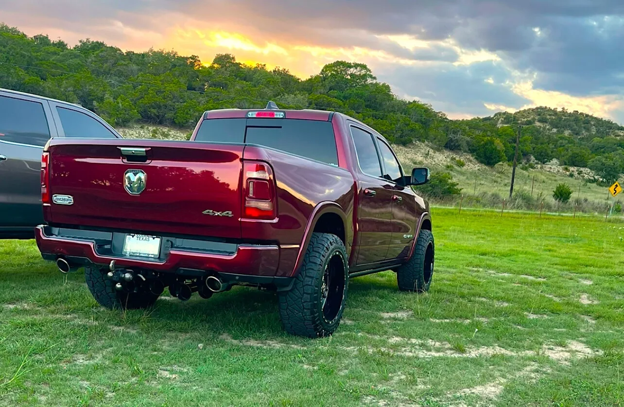 Rear angled view of a red Dodge Ram 1500 Longhorn with underbody train horn setup visible