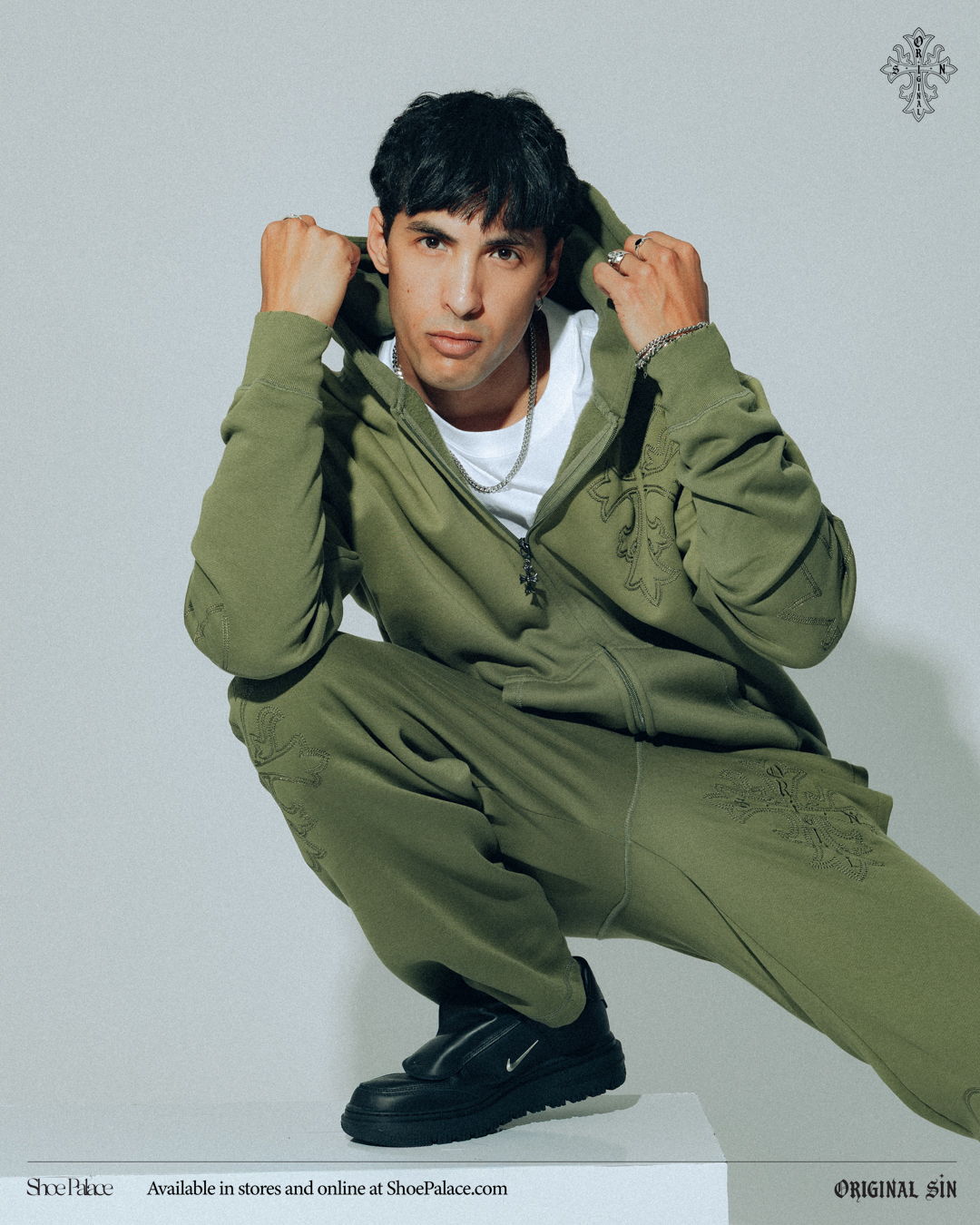 Person in olive green outfit squatting against a light background.