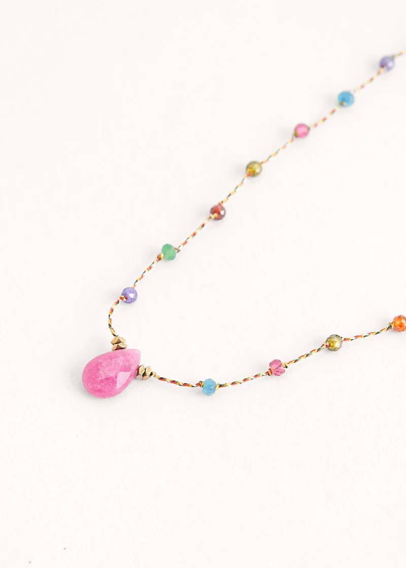 A necklace with a multicoloured thred chain with alternating colour spherical crystal beads and a pink teardrop pendant