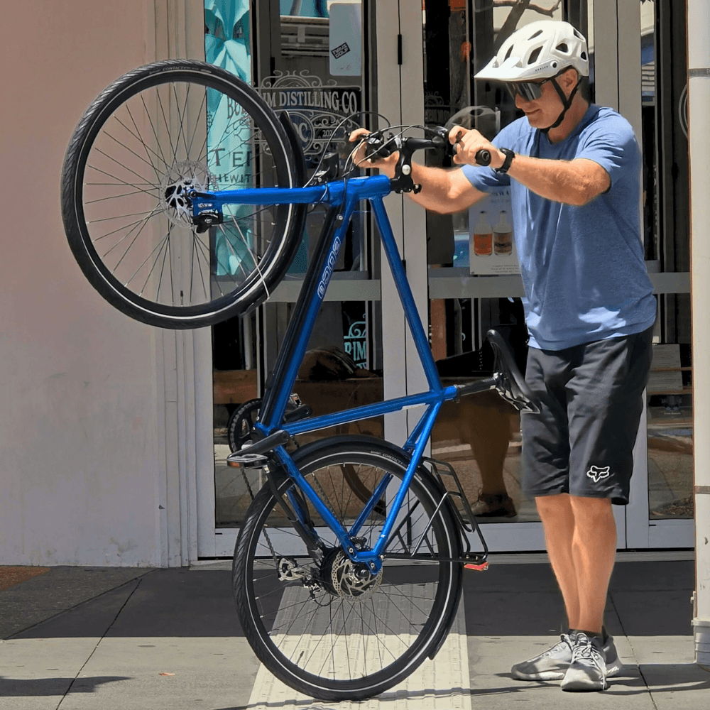 Person in helmet lifting a blue bicycle with the front wheel raised.