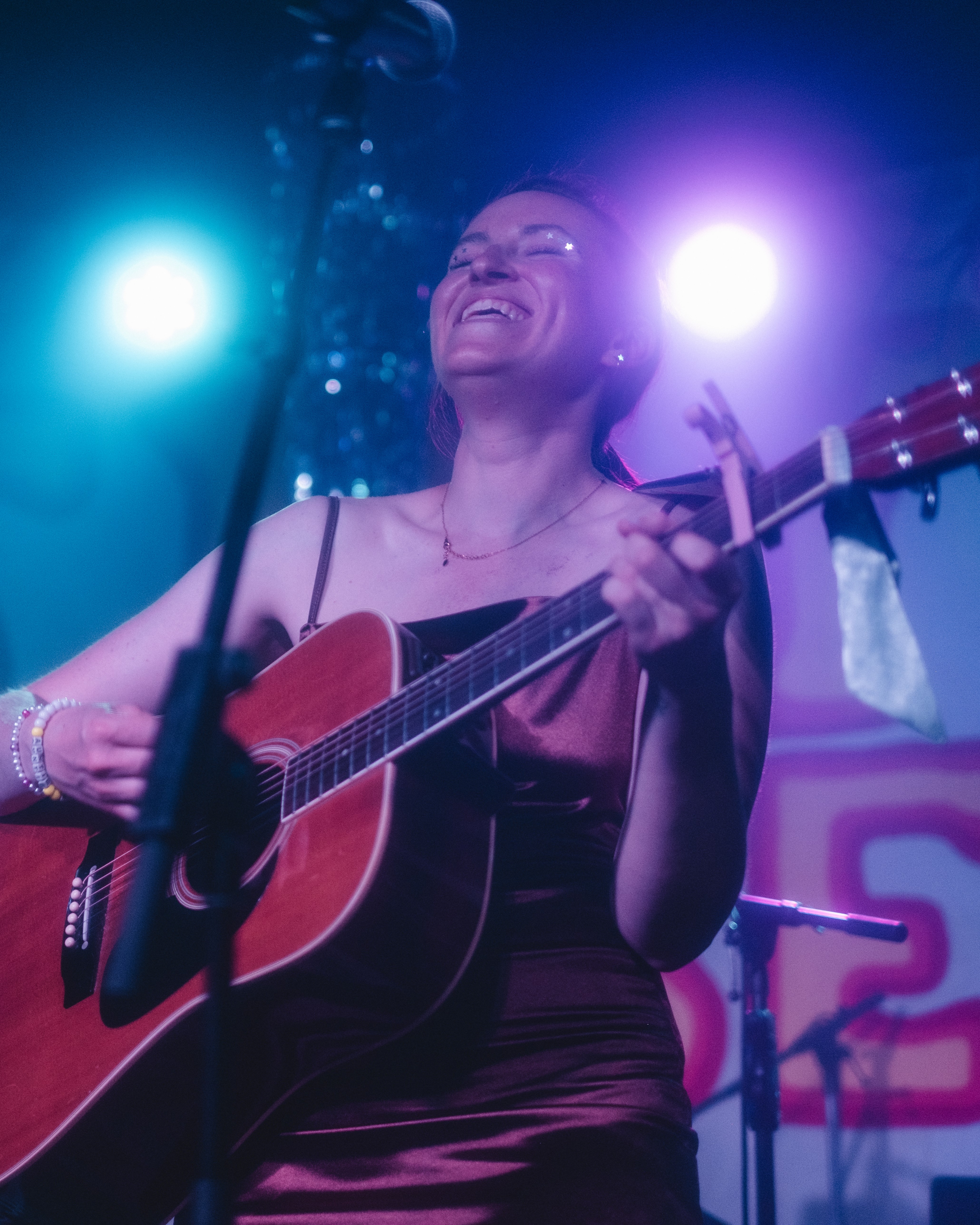 Woman playing acoustic guitar on stage with colorful lights.