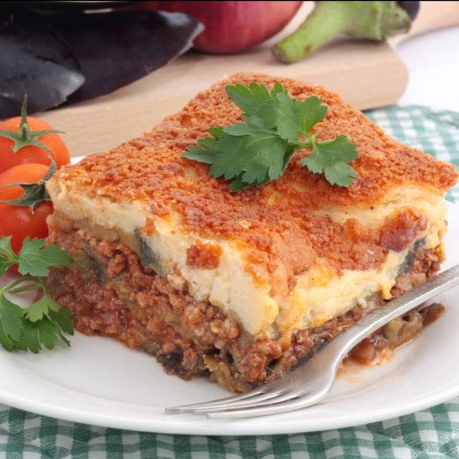 mousakka with bechamel sauce and parsley on top with a plate and fork