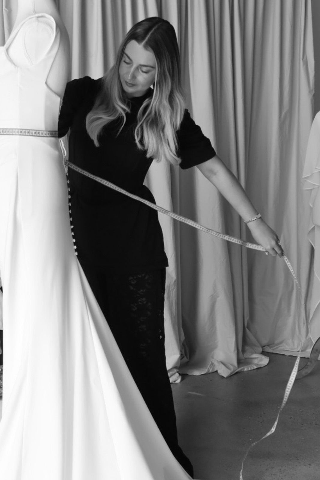 A fashion designer measuring a dress on a mannequin.