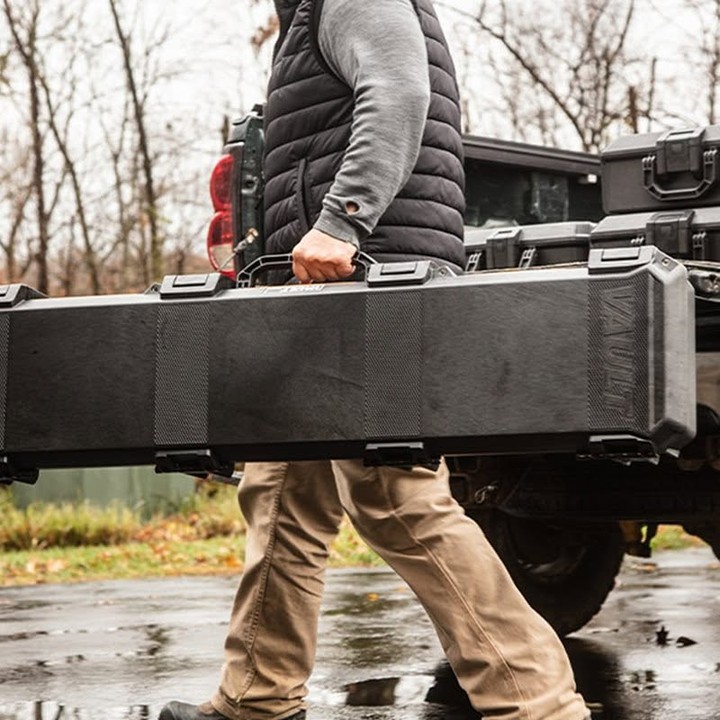 Person carrying a large black case near a vehicle in a wooded area.