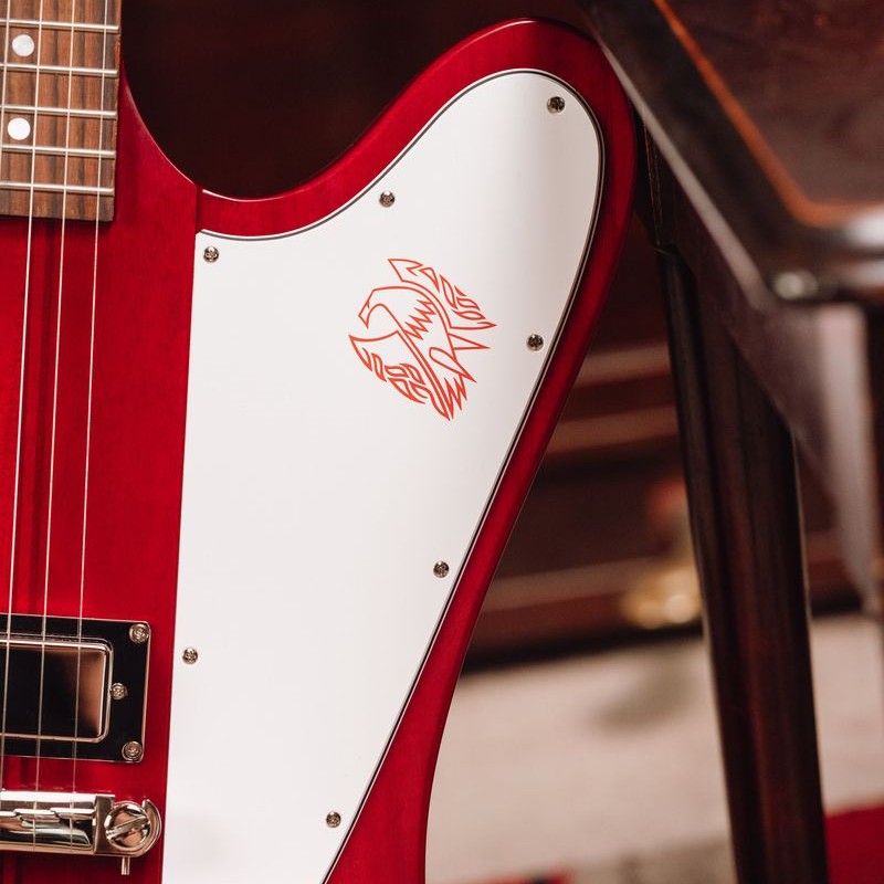 Close-up of a red guitar with a white pickguard and logo.