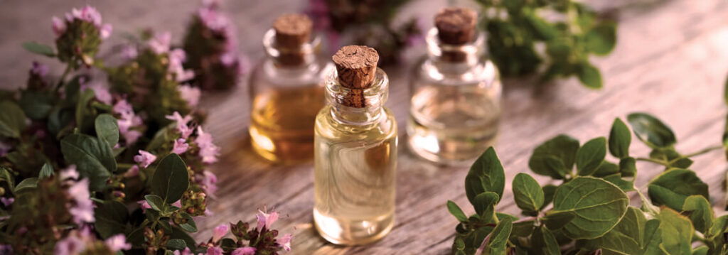 Bottles of essential oils with herbs and flowers in the background.