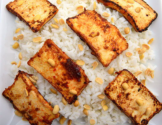 Fried tofu slices served over a bed of rice with peanuts.